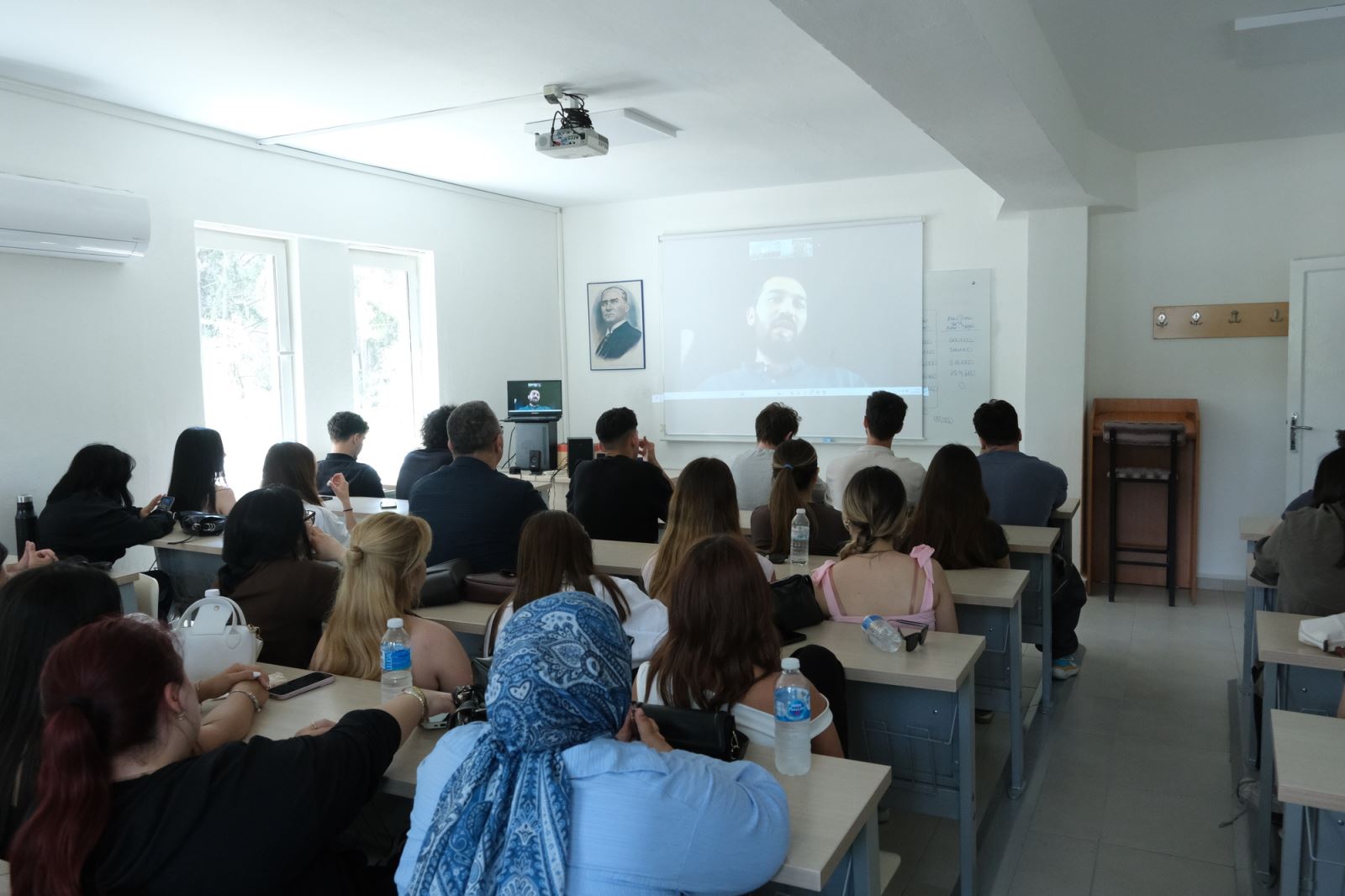 Derslikte öğrenciler sıralarda oturarak çevrim içi gerçekleştirilen kariyer konferansını izlemektedir.